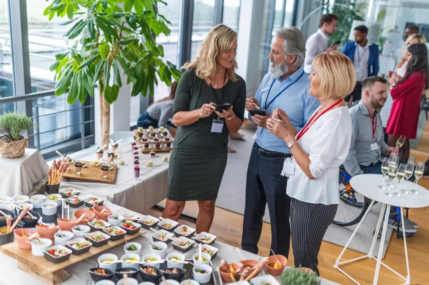 A group of people socializing around a table filled with food and drinks.