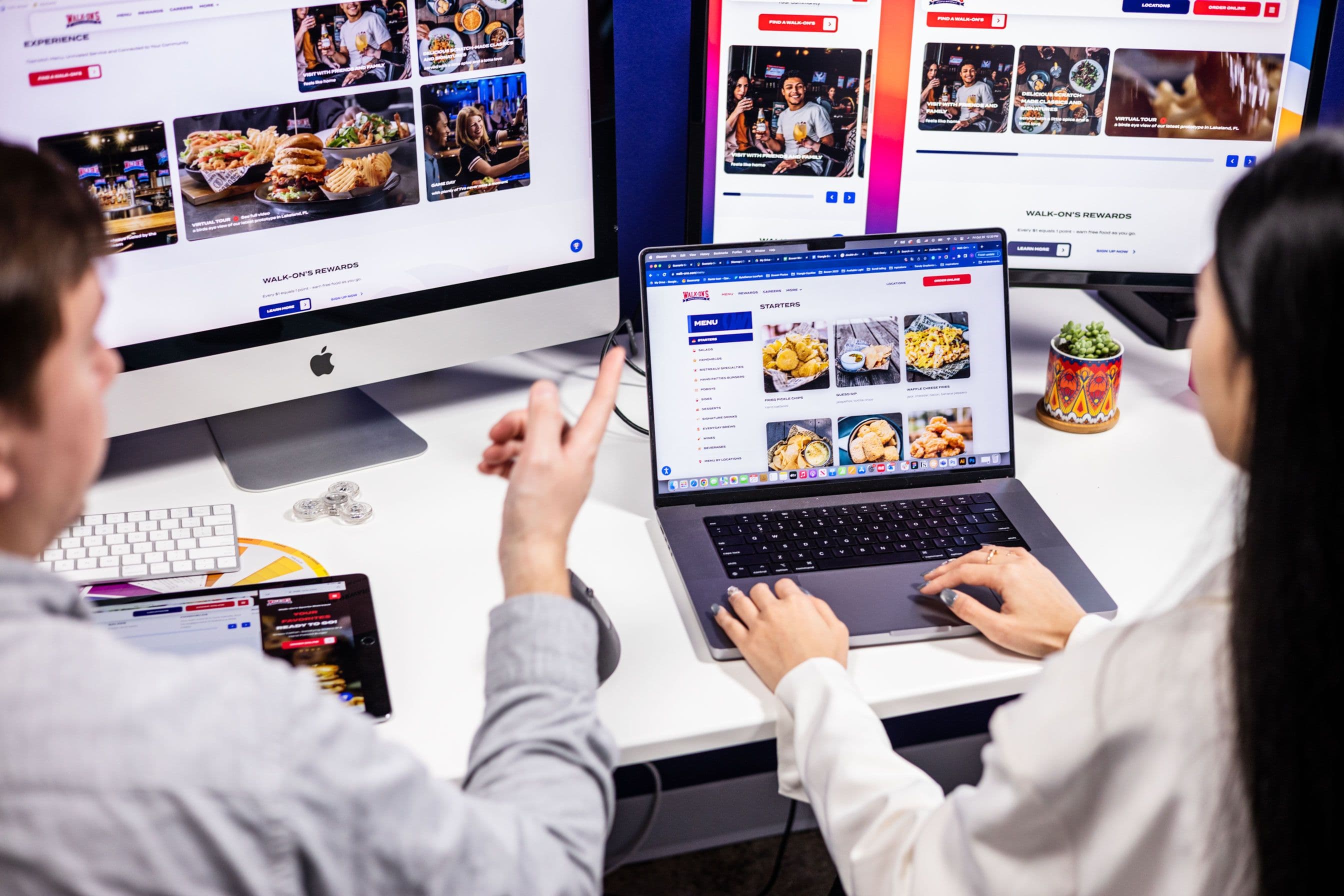 An image featuring two professionals using a laptop, desktop and iPad to look at different breakpoints of a website. Emphasizes website design and responsiveness