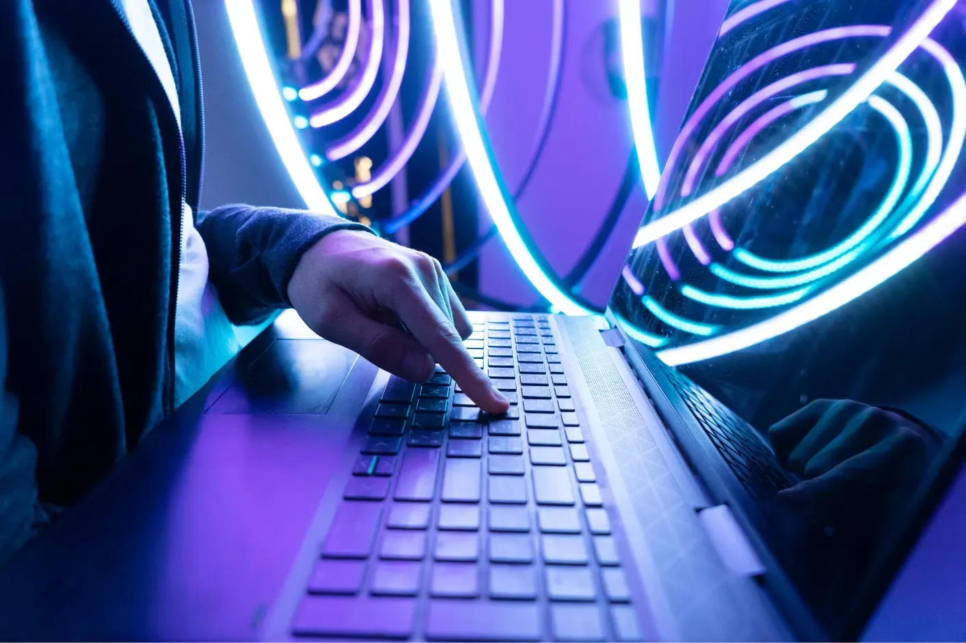 A person typing on a laptop with vibrant neon lights illuminating the surroundings.